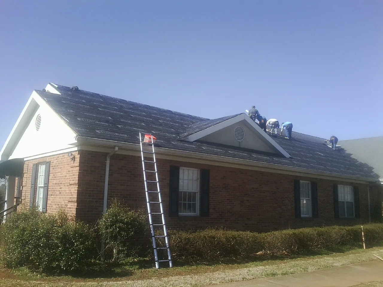 Crew tearing shingles off a brick ranch roof with a ladder set — Emergency Roof Repair work by our crew in Redwood