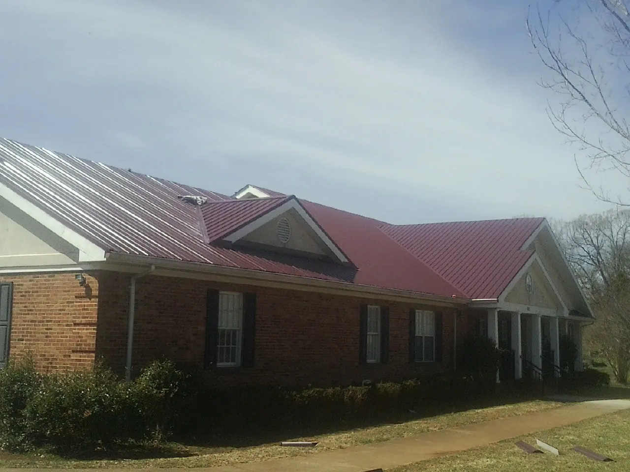 Red metal roof with gabled entries on a long brick building, from a Hail Damage Roof Repair job in Redwood