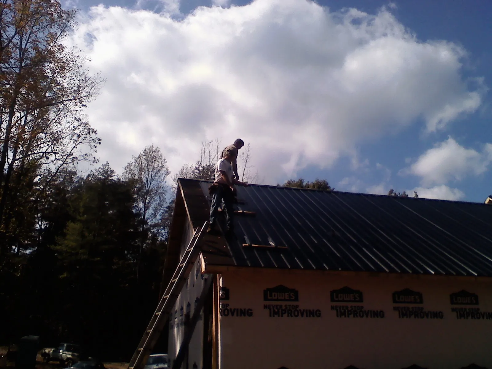 Roofer fastening dark metal panels high against a cloudy sky, from a Roof Inspection job in Redwood