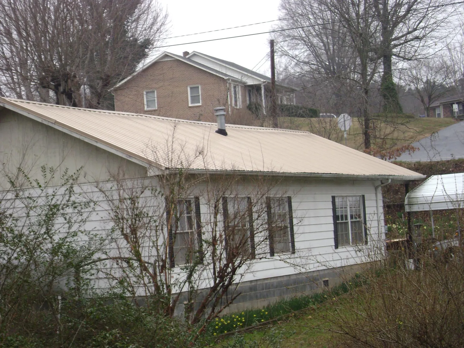 Tan metal roof on a white sided house set into a hillside — Commercial Roofing by Roofing Brothers in Redwood